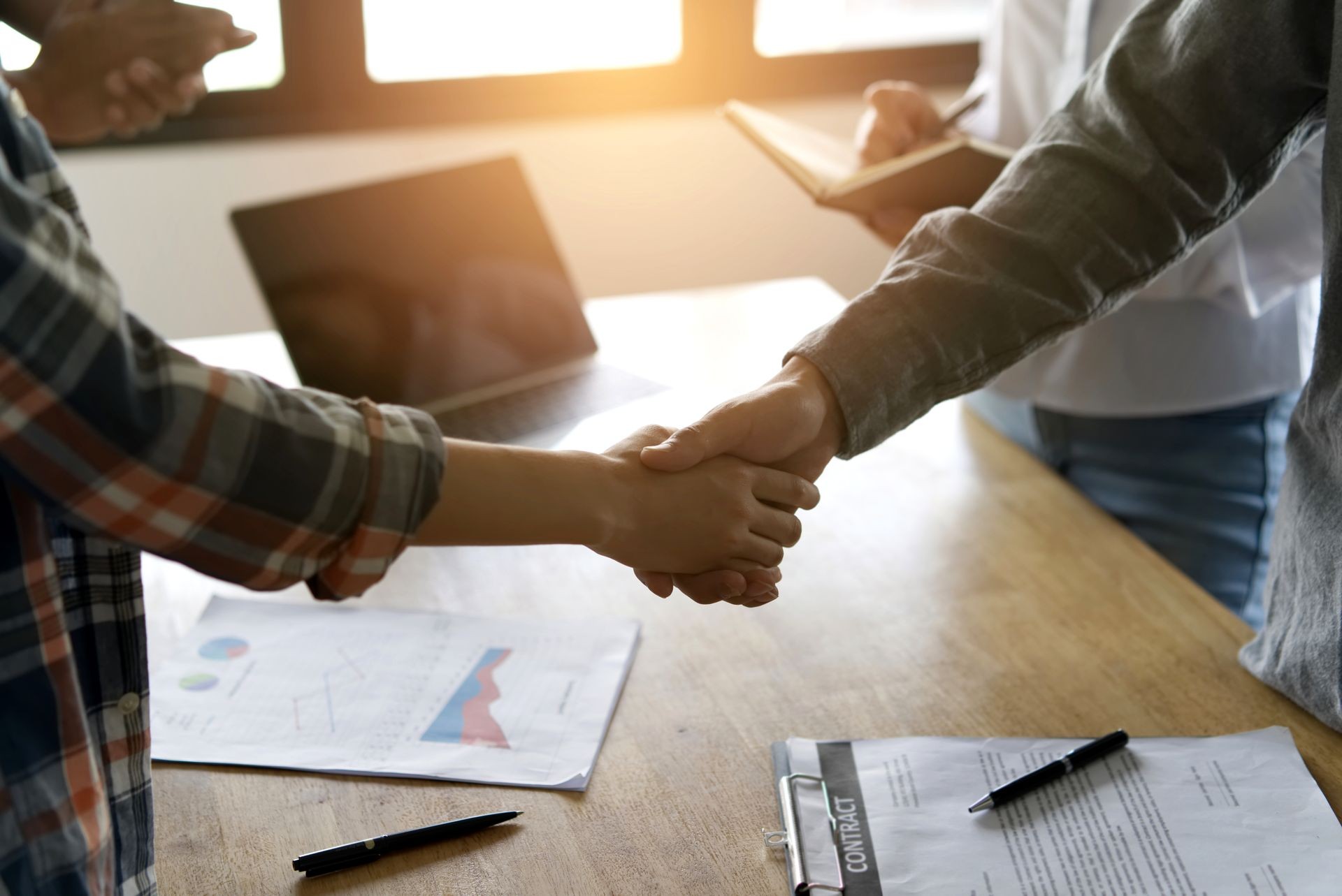 Two confident business partner shaking hands during a meeting in the office. Other members are clapping hands and  taking some note. Success, dealing, greeting and partner concept.